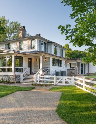 Side view of remodeled white house near Asheville, North Carolina, built by luxury home builder with energy-efficient features and original farmhouse aspects, showcasing locally milled wood and exposed beams.
